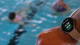 Smart Watch eines Schwimmmeisters im Vordergrund, dahinter unscharf das Schwimmbecken