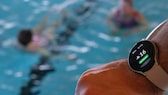 Smart Watch eines Schwimmmeisters im Vordergrund, dahinter unscharf das Schwimmbecken