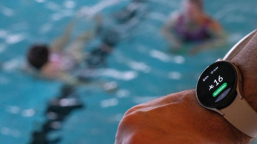 Smart Watch eines Schwimmmeisters im Vordergrund, dahinter unscharf das Schwimmbecken