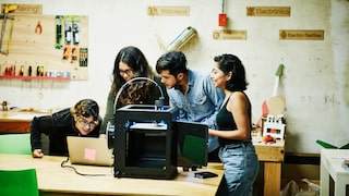 4 Menschen stehen vor einem 3D-Drucker und einem Laptop.