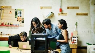 4 Menschen stehen vor einem 3D-Drucker und einem Laptop.