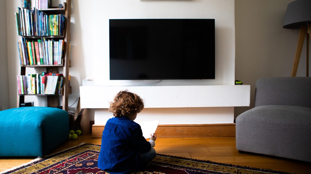 Kleiner Junge sitzt auf dem Boden vor einem Fernseher.