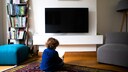 Kleiner Junge sitzt auf dem Boden vor einem Fernseher.
