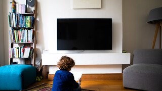 Kleiner Junge sitzt auf dem Boden vor einem Fernseher.