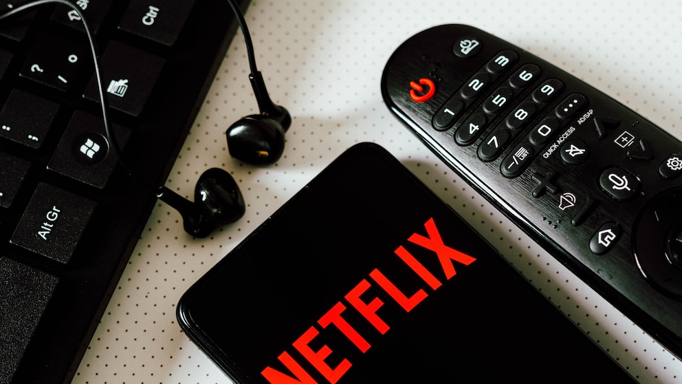 Netflix Account Sharing Gebühr Folgen: Netflix Logo auf Smartphone neben Fernbedienung und Computertatstatur