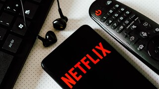 Netflix Account Sharing Gebühr Folgen: Netflix Logo auf Smartphone neben Fernbedienung und Computertatstatur