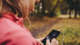 Frau im Park checkt ihre Selftracking App auf dem Smartphone