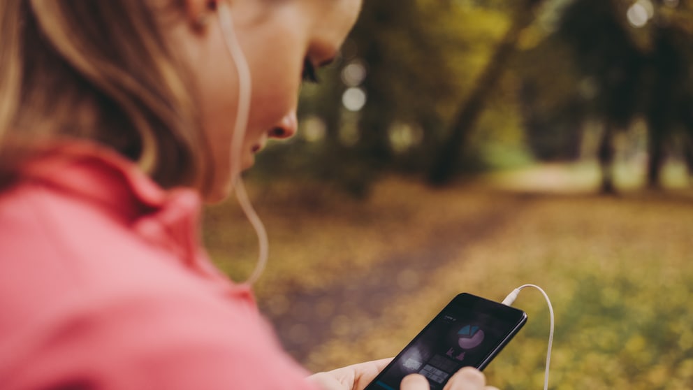 Frau im Park checkt ihre Selftracking App auf dem Smartphone