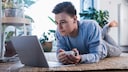 Mann liegt auf dem Boden und schaut ein Video auf seinem Laptop