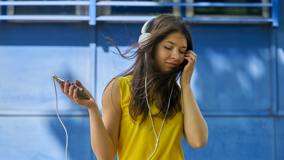 Frau im gelben T-Shirt hört Musik übers Smartphone.