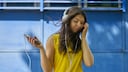 Frau im gelben T-Shirt hört Musik übers Smartphone.
