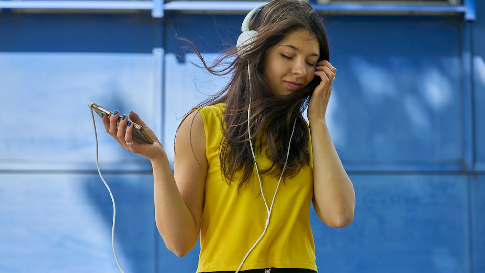 Frau im gelben T-Shirt hört Musik übers Smartphone.