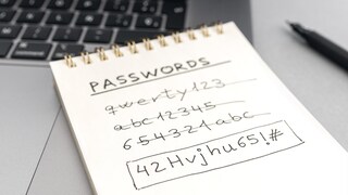 Symbolbild: Zettel mit mehreren, durchgestrichenen Passwörtern vor einem Laptop.