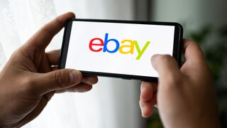 Symbolbild: Zwei Hände halten ein Smartphone, das den Schriftzug „Ebay“ trägt