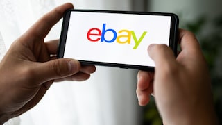 Symbolbild: Zwei Hände halten ein Smartphone, das den Schriftzug „Ebay“ trägt