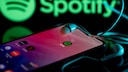 Symbolbild: Spotify-App auf Smartphone und im Hintergrund das Logo.