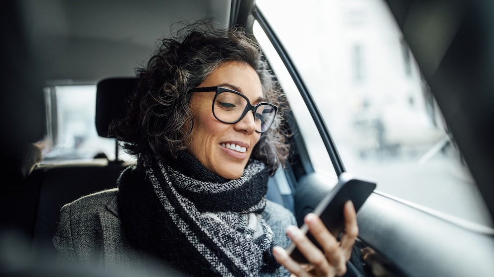Frau schaut beim Autofahren auf ihr Smartphone in ihrer Hand.