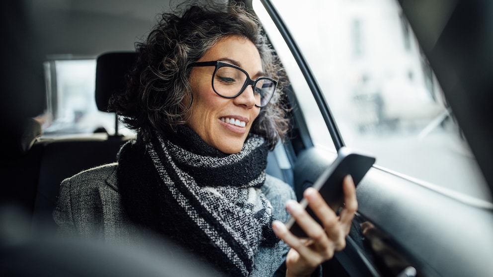 Frau schaut beim Autofahren auf ihr Smartphone in ihrer Hand.