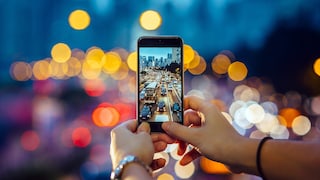 Symbolbild: Frau fotografiert mit Smartphone den abendlichen Verkehr, der mit Bokeh-Effekt im Hintergrund zu sehen ist.