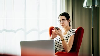 Young woman sitting down scrolling through her phone in a hotel room.