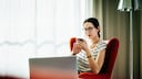 Young woman sitting down scrolling through her phone in a hotel room.