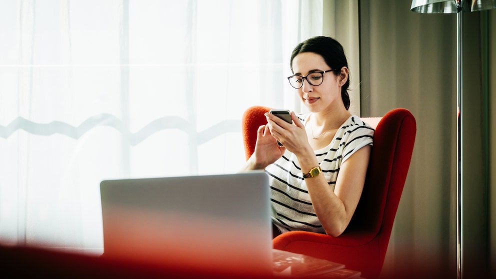 Young woman sitting down scrolling through her phone in a hotel room.