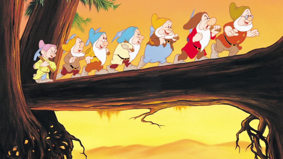 Ausschnitt aus dem Disney-Film „Schneewittchen und die sieben Zwerge“, das die Zwerge über eine Baumstamm-Brücke laufend zeigt.