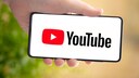 Symbolbild: Hand hält Smartphone mit YouTube-Startbildschirm