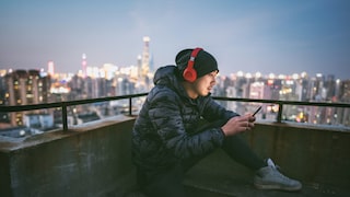 Man sitzt mit roten Kopfhörer und Smartphone