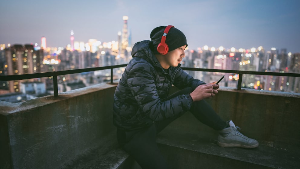 Man sitzt mit roten Kopfhörer und Smartphone