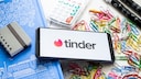 Tinder Logo auf einem Smartphone mit Bürosachen im Hintergrund