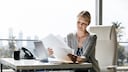 Frau mit viel Papier vor dem Laptop.