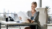 Frau mit viel Papier vor dem Laptop.