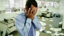 Mann hält sich im unordentlichen Büro die Hände vor dem Gesicht