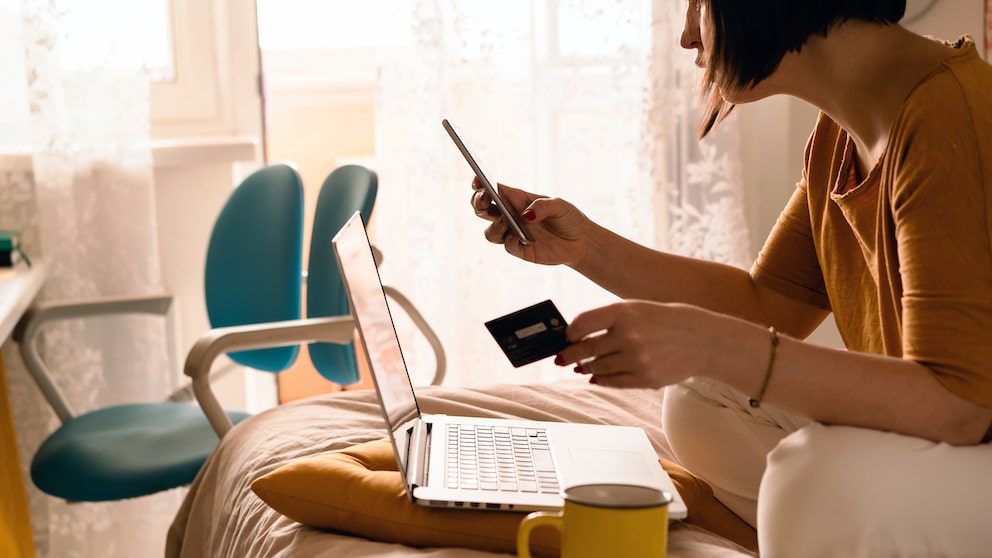 Symbolbild: Frau sitzt auf dem Sofa und gibt an ihrem Laptop ihre Zahlungsdaten ein.