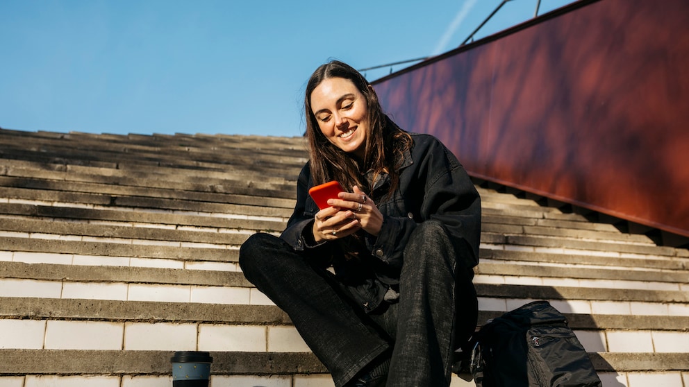 Symbolbild: junge Frau sitzt draußen und beschäftigt sich mit ihrem Smartphone