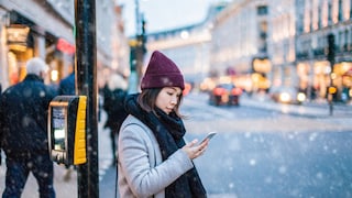 Junge Frau nutzt bei Schnee und Kälte Smartphone