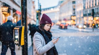 Junge Frau nutzt bei Schnee und Kälte Smartphone