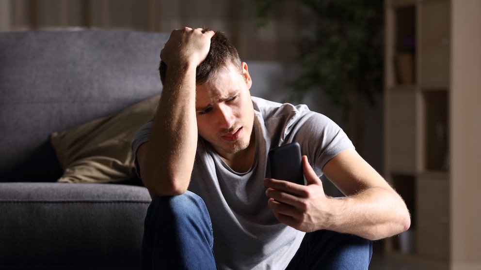 Symbolbild: Junger Mann schaut besorgt auf sein Smartphone.