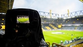 Symbolbild: Blick auf ein Fußballstadium durch eine Filmkamera.