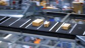 Symbolbild: drei Pakete auf einem Fließband in einem Paketzentrum.