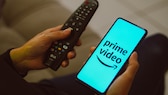 Amazon prime Video Werbung Logo des Dienstes auf Smartphone neben Fernbedienung fü TV