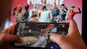 Person spielt "Fortnite" auf dem Hany, im Hintergrund ist ein Wallpaper zum Spiel zu sehen.