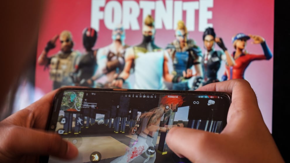 Person spielt "Fortnite" auf dem Hany, im Hintergrund ist ein Wallpaper zum Spiel zu sehen.