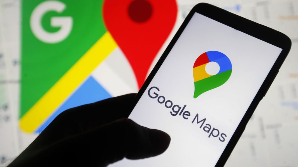 Person hält Handy mit Google-Maps-Logo auf dem Display, im Hintergrund ist die App offen.