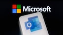 Handy mit Outlook-Icon auf dem Display, im Hintergrund das Microsoft-Logo.