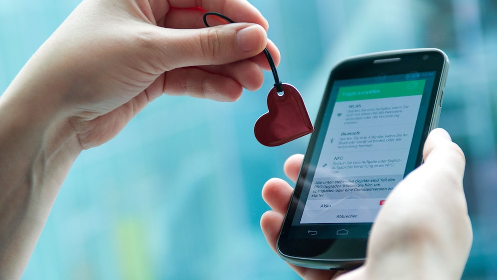 Symbolbild: Eine Hand zeigt einen herzförmigen NFC-Anhänger vor einem Smartphone