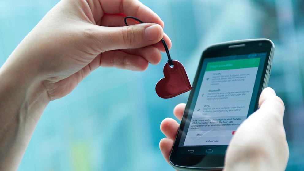 Symbolbild: Eine Hand zeigt einen herzförmigen NFC-Anhänger vor einem Smartphone