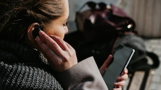 Frau mit Handy in der Hand und In Ear Kopfhörer im Ohr