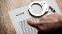 Person zeigt auf einen Zettel mit einer polizeilichen Anzeige und einer Handschelle.